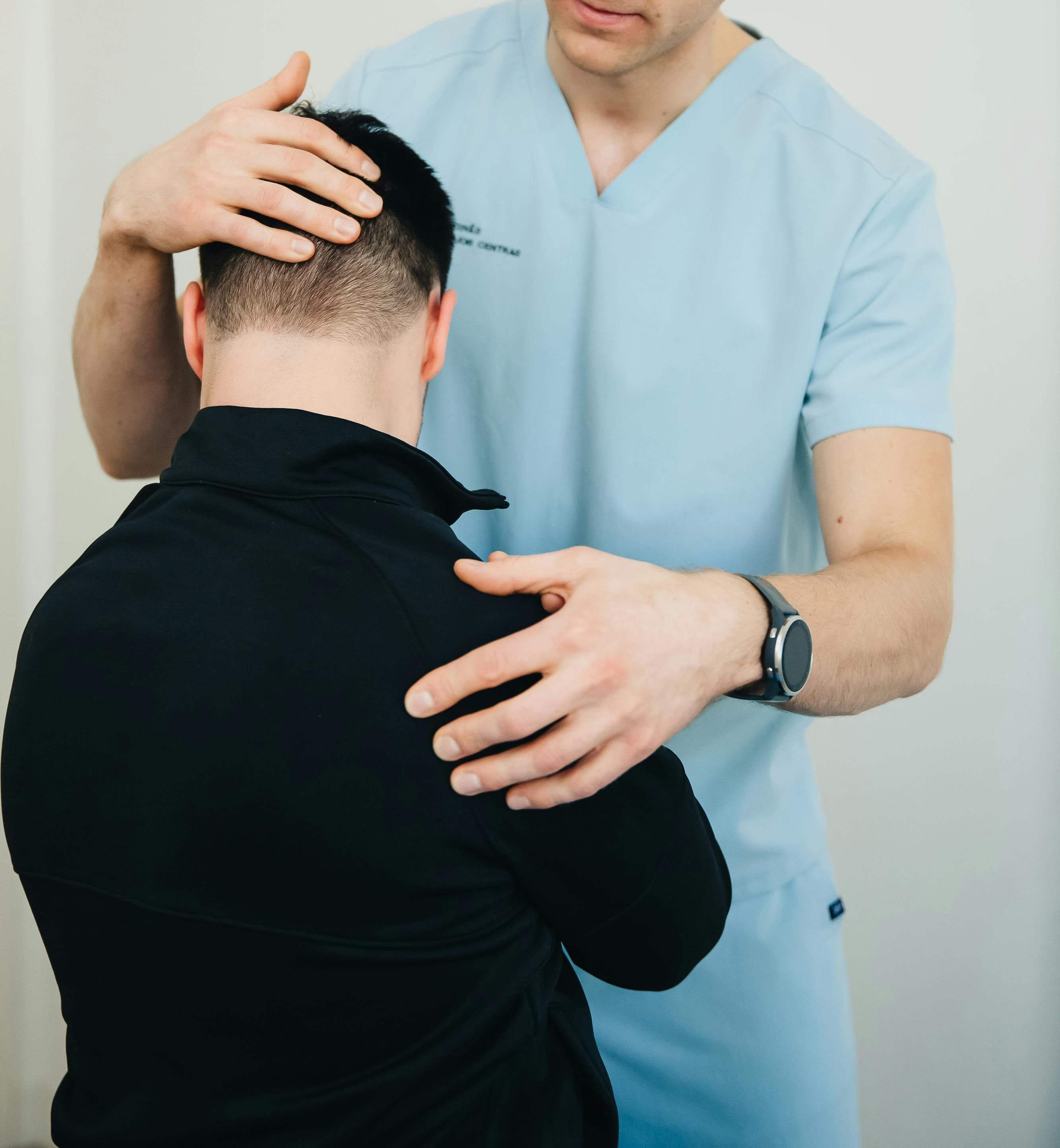 Een zorgverlener in blauwe kleding ondersteunt voorzichtig het hoofd en de nek van een patiënt tijdens een sessie kinesitherapie.